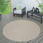 Moderne patio met rond geweven kleed, donkere meubels en plant, ideaal voor buiten ontspanning.
